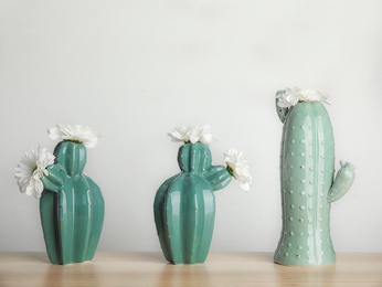 Photo of Trendy cactus shaped vases with flowers on table against light wall. Creative decor