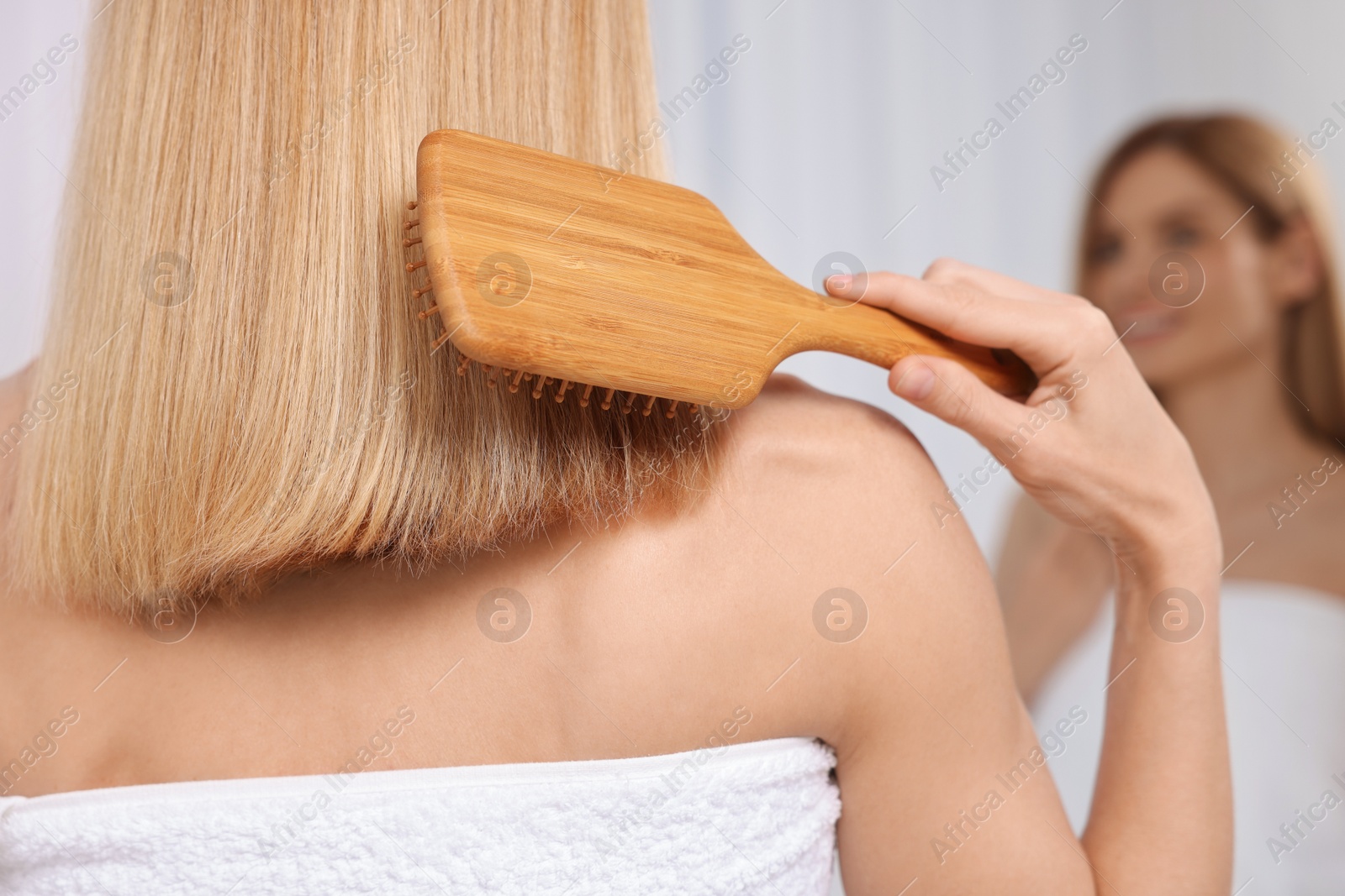 Photo of Woman brushing her hair near mirror in room, back view