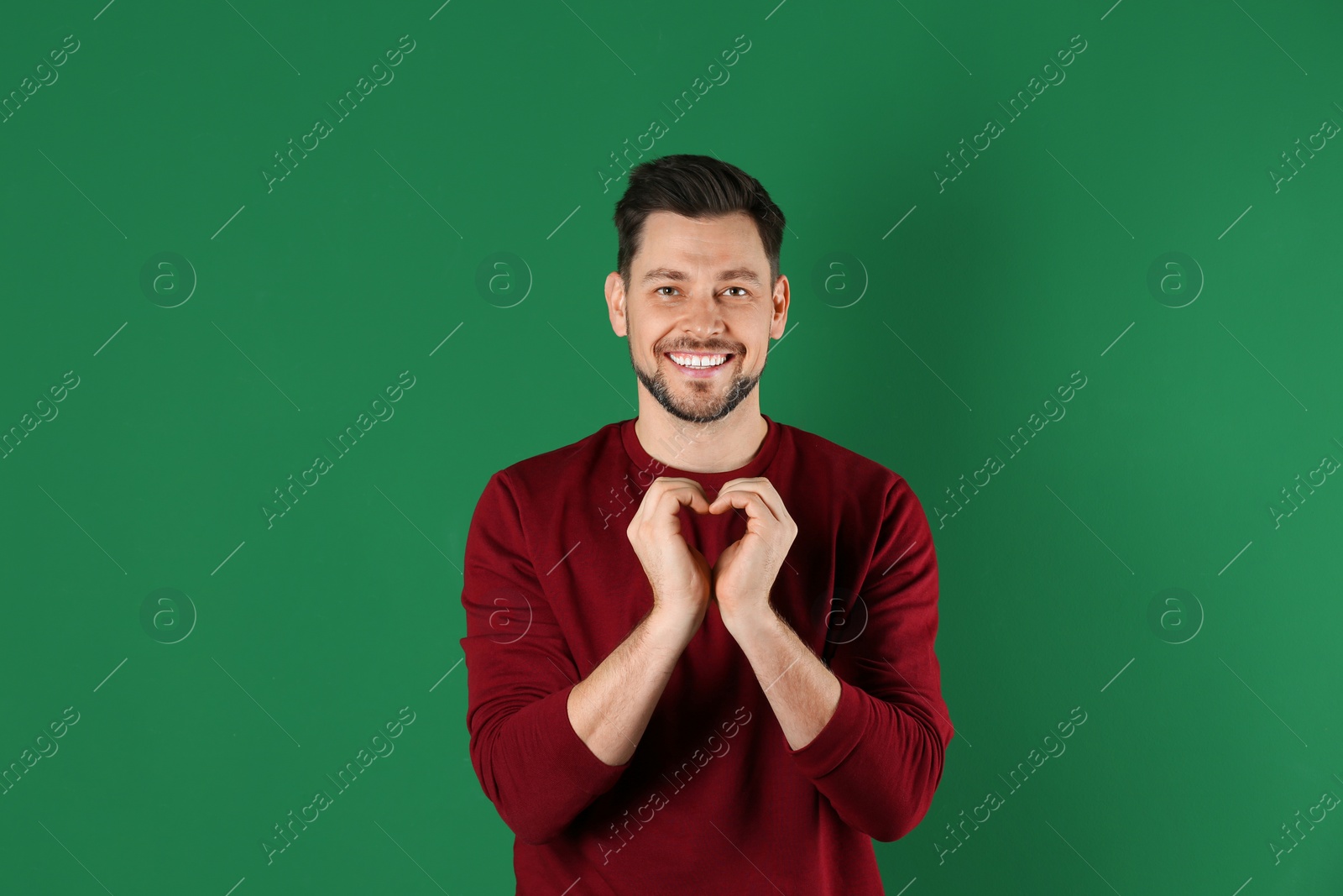 Photo of Portrait of handsome man making heart with his hands on color background