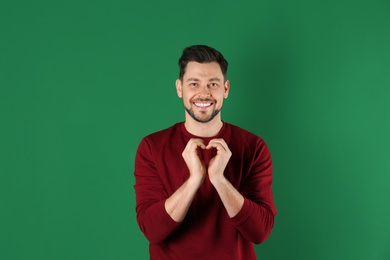 Portrait of handsome man making heart with his hands on color background