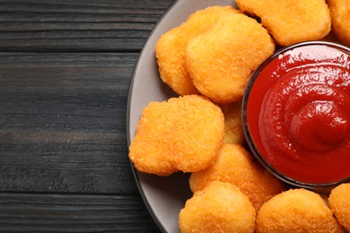 Photo of Tasty fried chicken nuggets with tomato sauce on black wooden table, top view