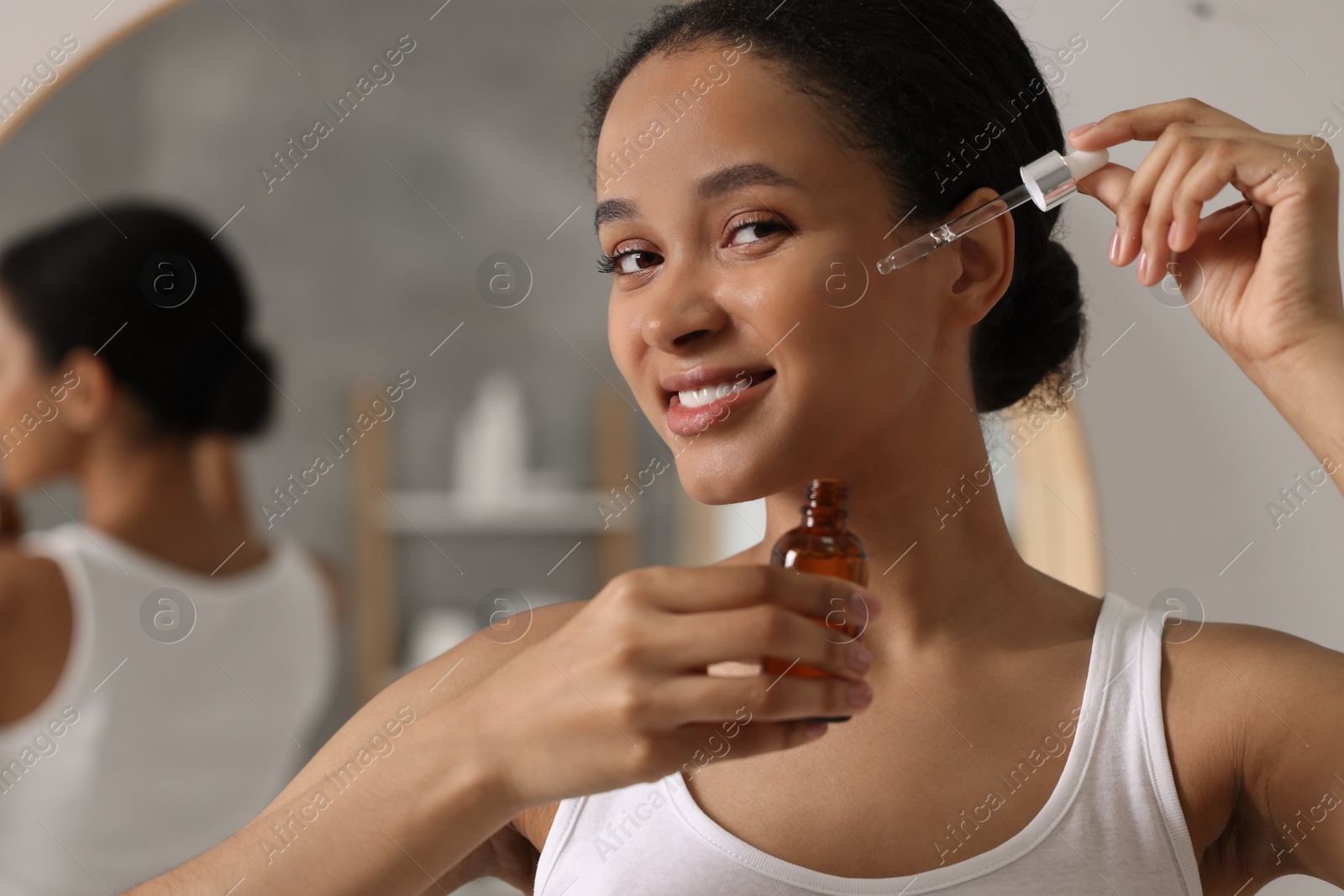 Photo of Smiling woman applying serum onto her face in bathroom