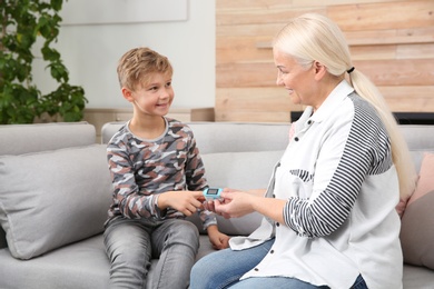 Photo of Mature woman checking little boy's pulse with medical device at home