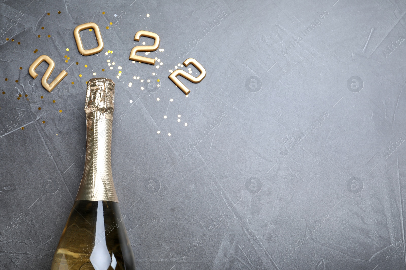 Photo of Bottle of sparkling wine, gold confetti and number 2022 on grey background, flat lay with space for text. Happy New Year