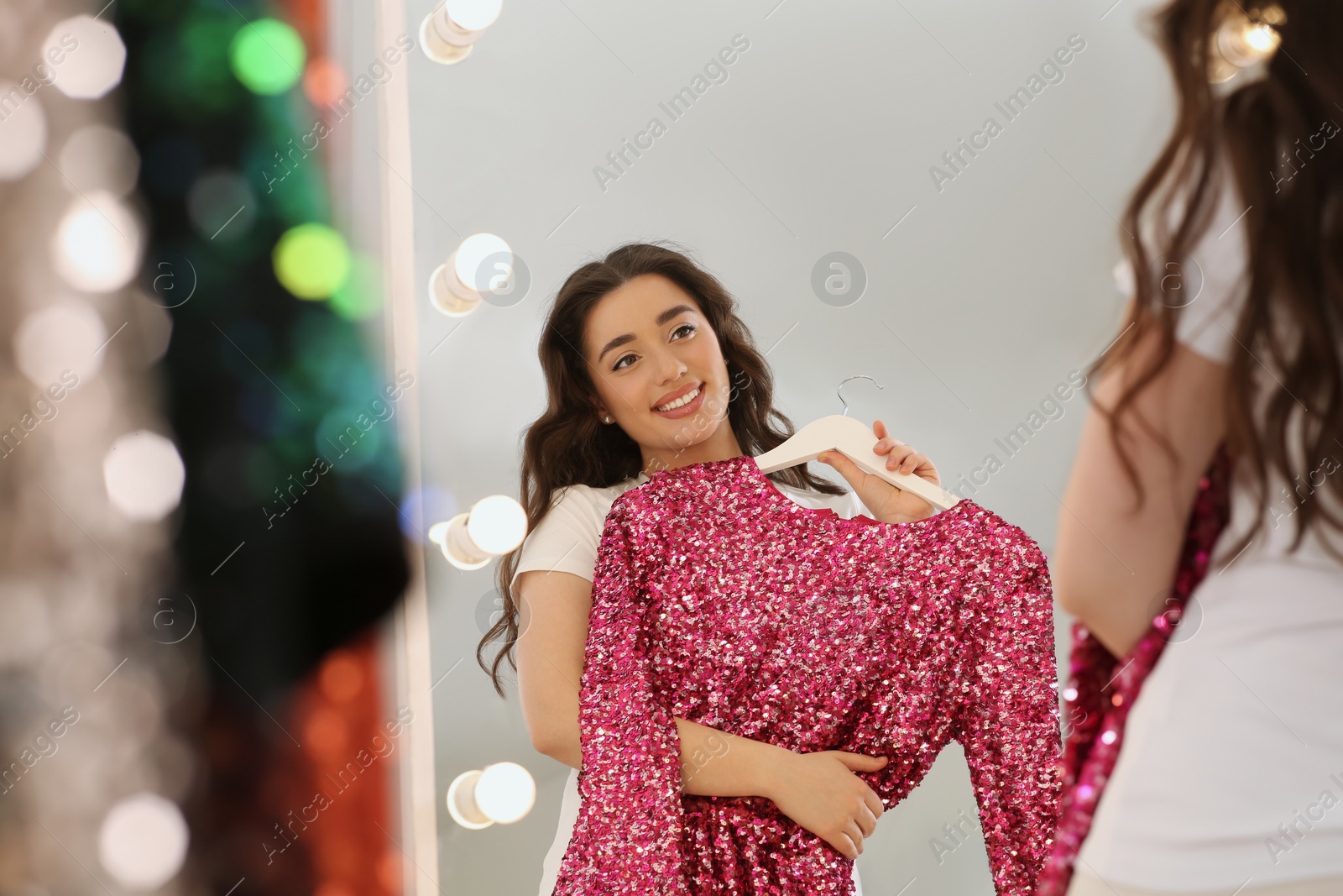 Photo of Beautiful young woman with pink sequin dress near mirror in boutique. Choosing party clothes