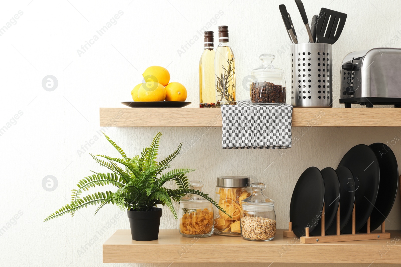 Photo of Wooden shelves with dishware and products on white wall. Kitchen interior idea