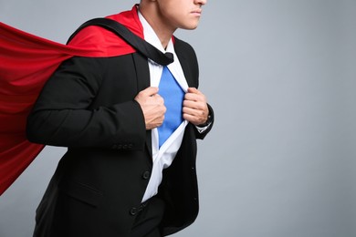 Photo of Businessman in superhero cape taking suit off on grey background, closeup. Space for text