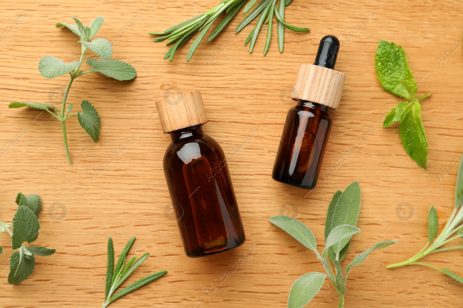 Photo of Bottles of essential oils and fresh herbs on wooden table, flat lay