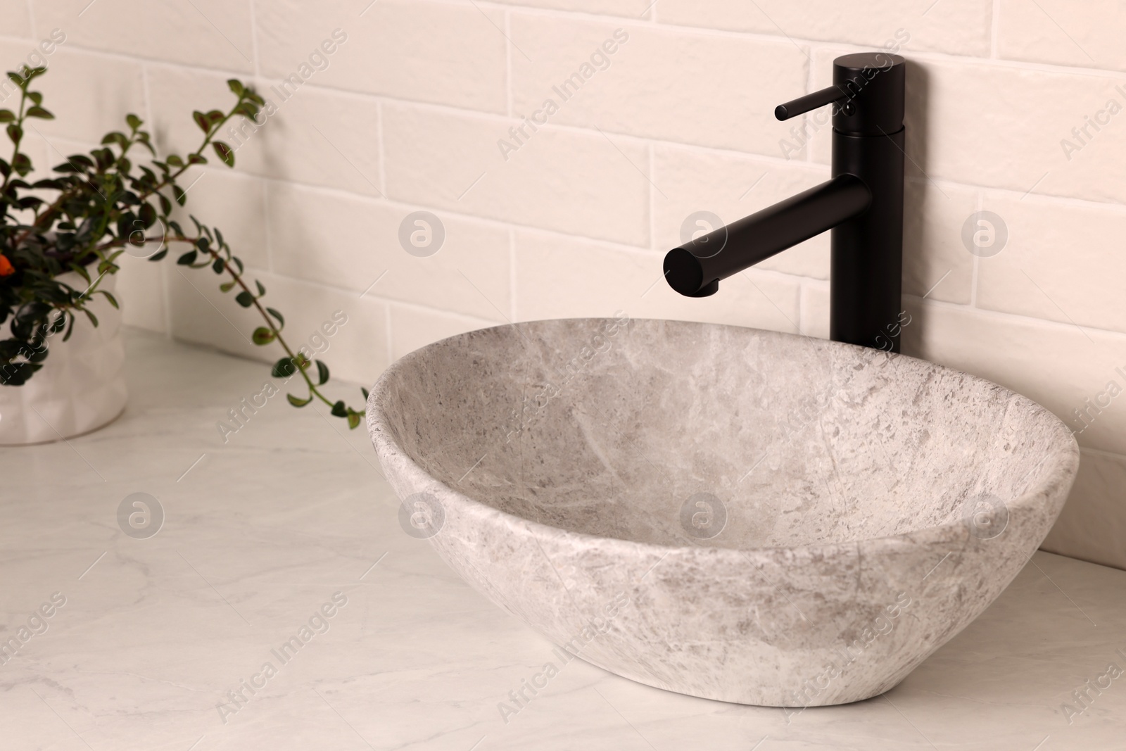 Photo of Stone vessel sink with faucet on white marble countertop