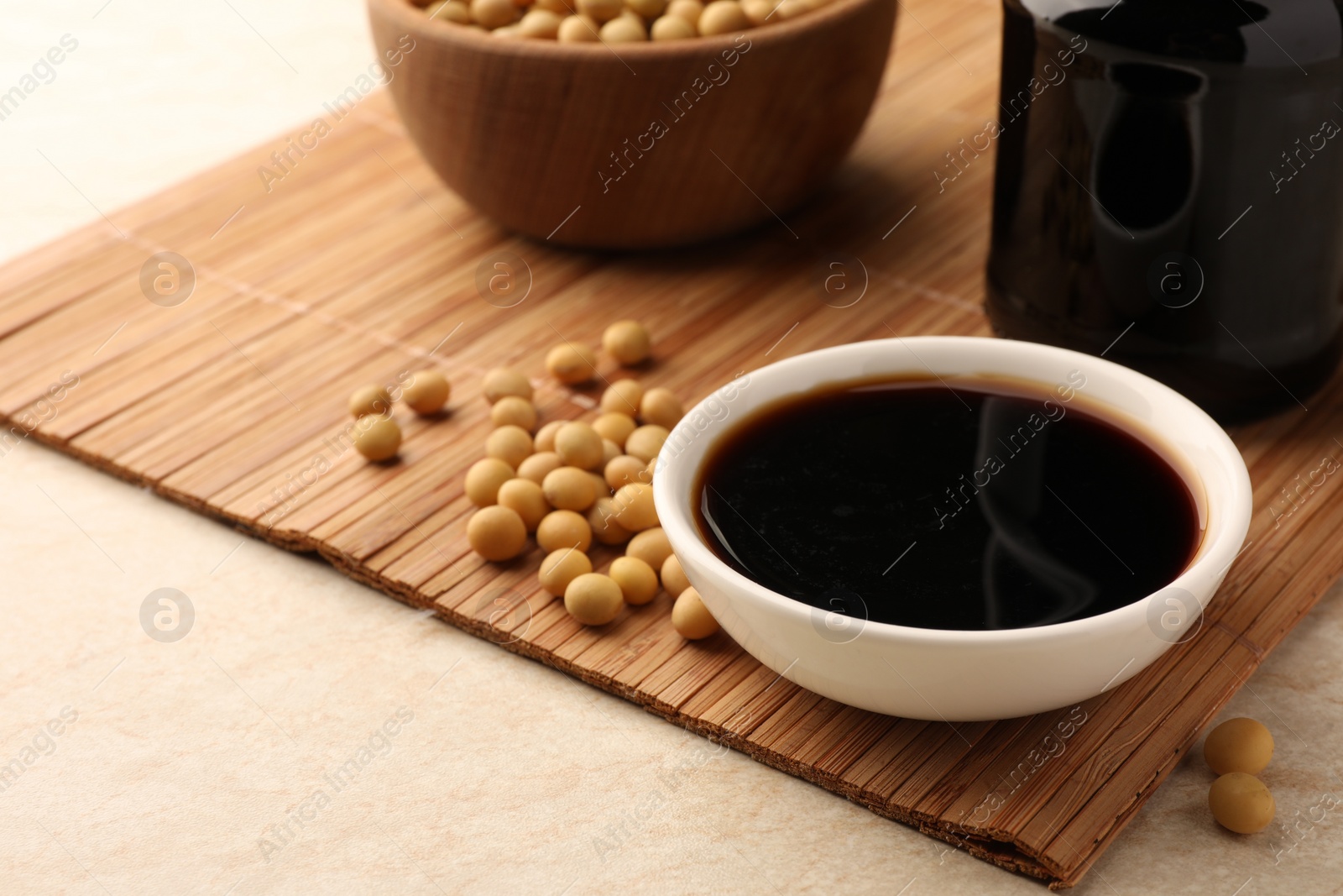 Photo of Soy sauce in bowl and soybeans on bamboo mat, closeup