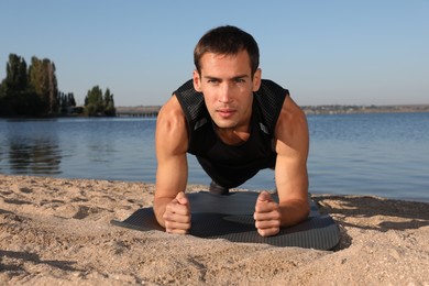Photo of Sporty man doing plank exercise on beach