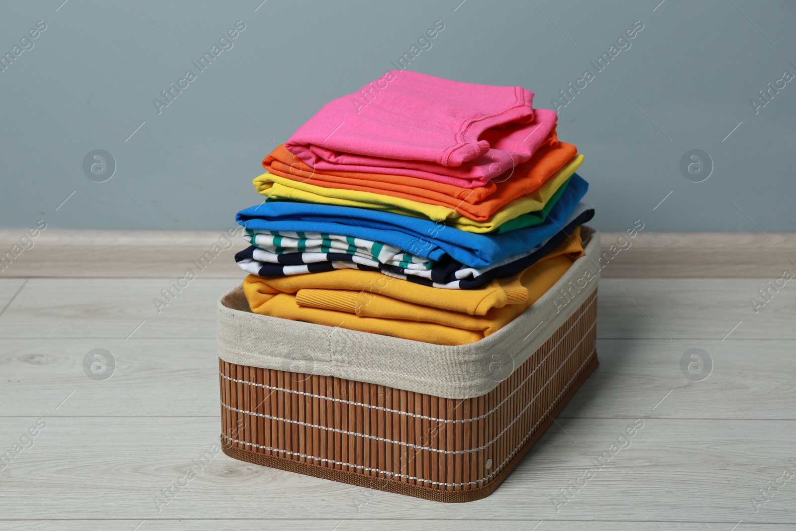 Photo of Laundry basket with clean stacked clothes on floor near grey wall