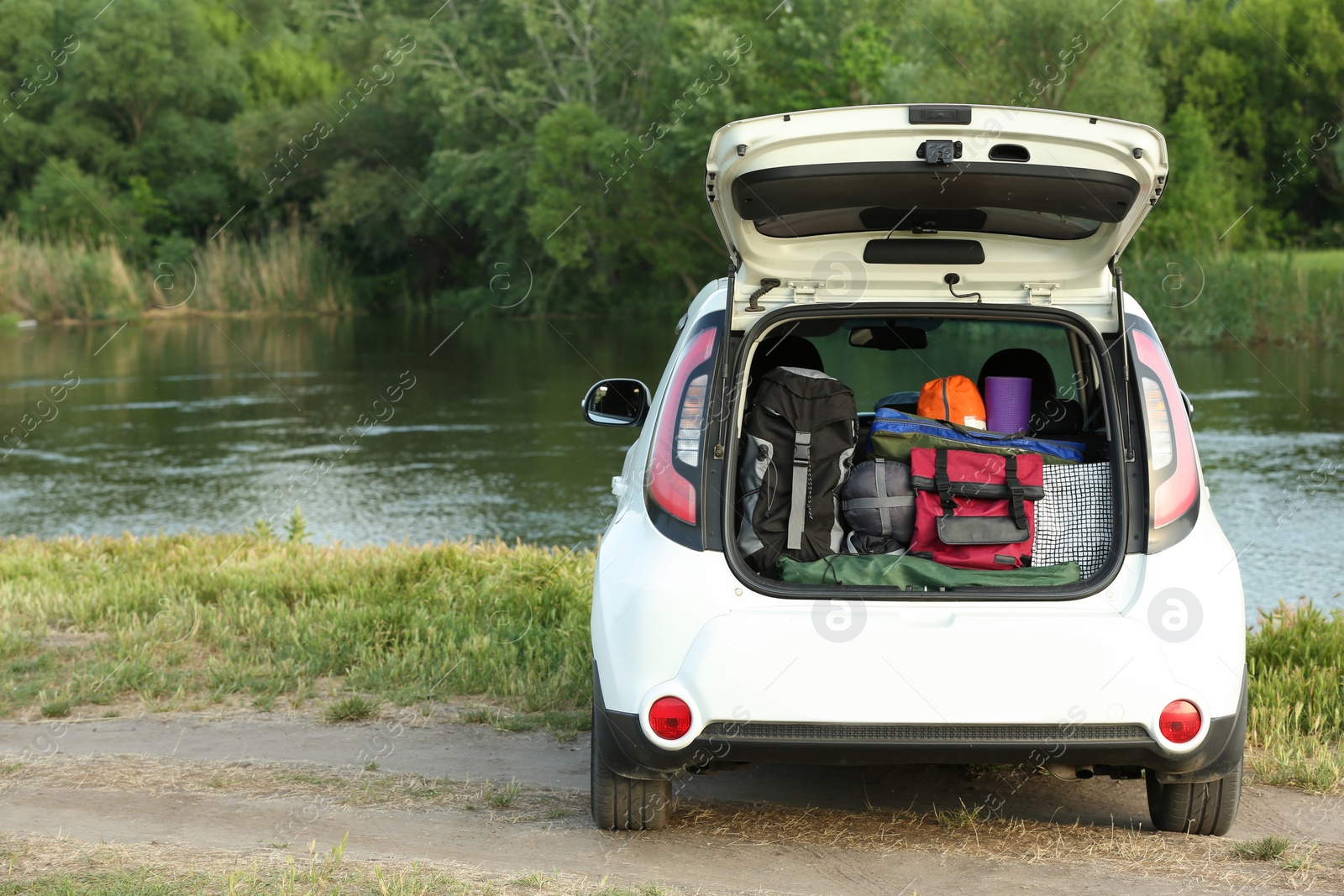 Photo of Car with camping equipment in trunk on riverbank. Space for text