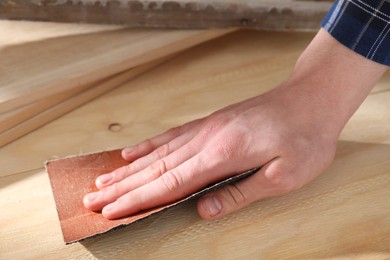 Photo of Man polishing wooden planks with sandpaper, closeup