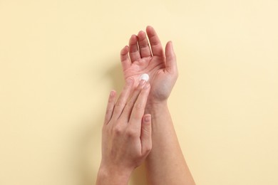 Woman applying cosmetic cream onto hand on beige background, top view