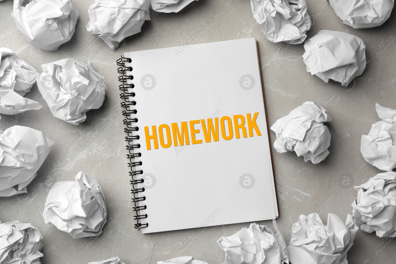 Image of Notebook with inscription HOMEWORK and crumpled paper balls on grey marble table, flat lay