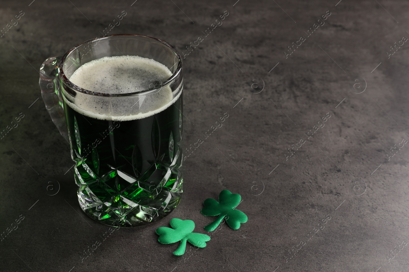 Photo of St. Patrick's day celebration. Green beer with decorative clover leaves on grey table. Space for text