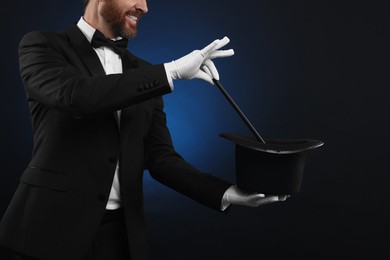 Photo of Magician showing magic trick with top hat on dark blue background, closeup