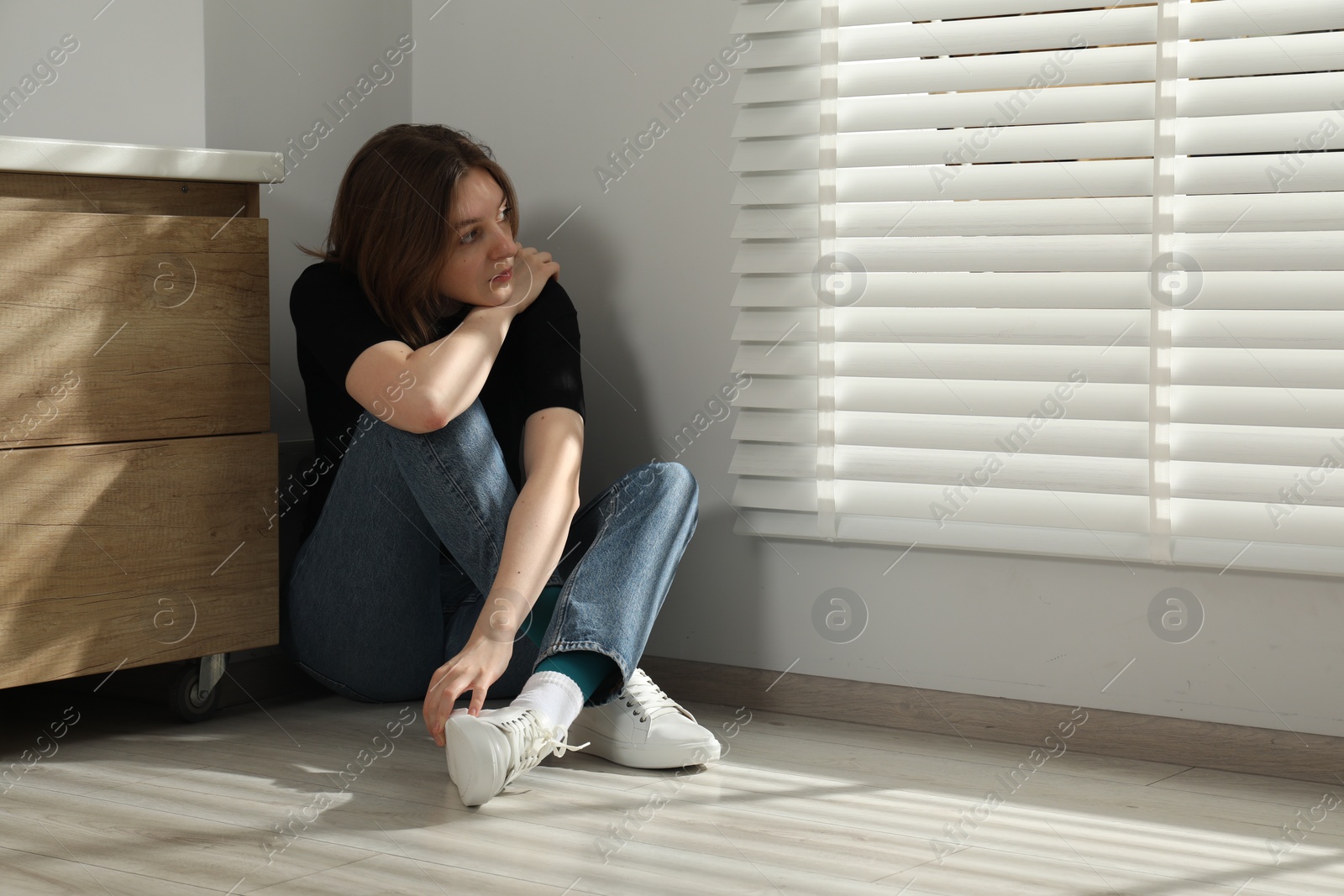 Photo of Sad young woman sitting on floor indoors, space for text