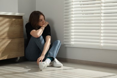 Sad young woman sitting on floor indoors, space for text