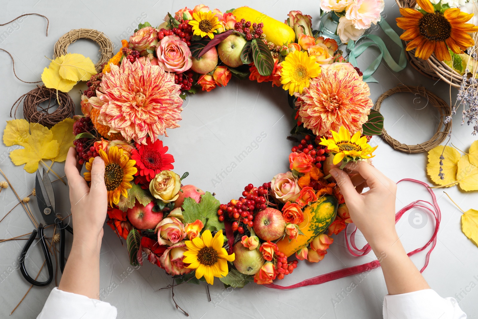 Photo of Florist making beautiful autumnal wreath with flowers and fruits at light grey table, top view