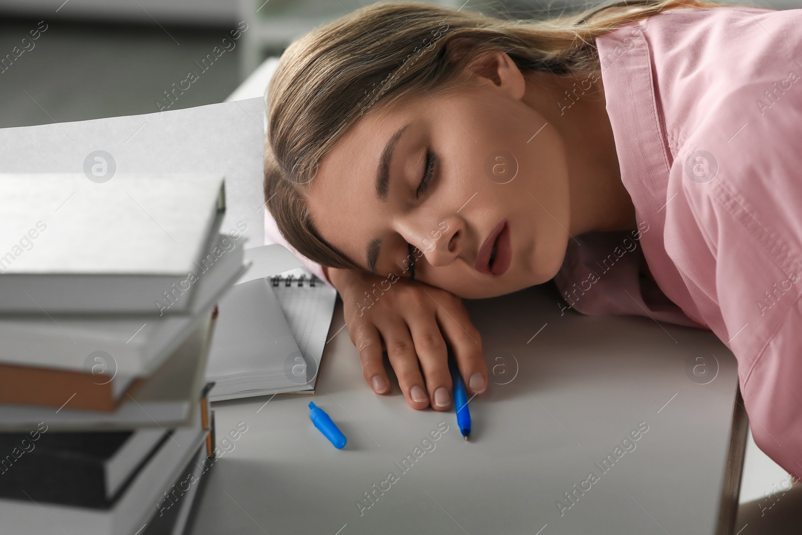 Photo of Young tired woman sleeping near books at white table indoors, closeup