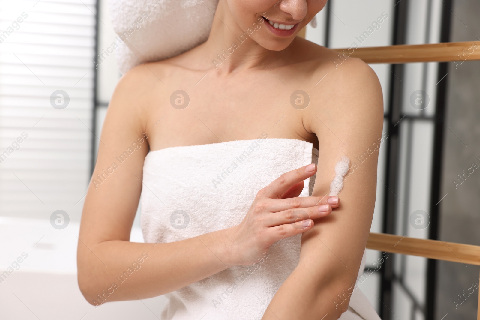 Photo of Woman applying self-tanning product onto arm indoors, closeup