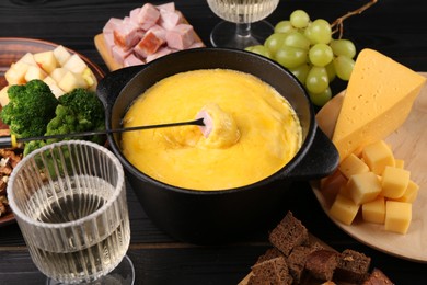 Photo of Fondue pot with melted cheese, fork and different products on black wooden table