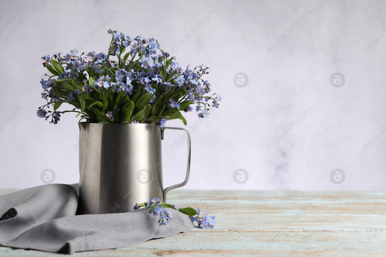 Photo of Beautiful forget-me-not flowers and napkin on wooden rustic table against light background, closeup. Space for text