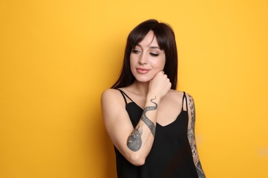Photo of Beautiful woman with tattoos on arms against yellow background. Space for text
