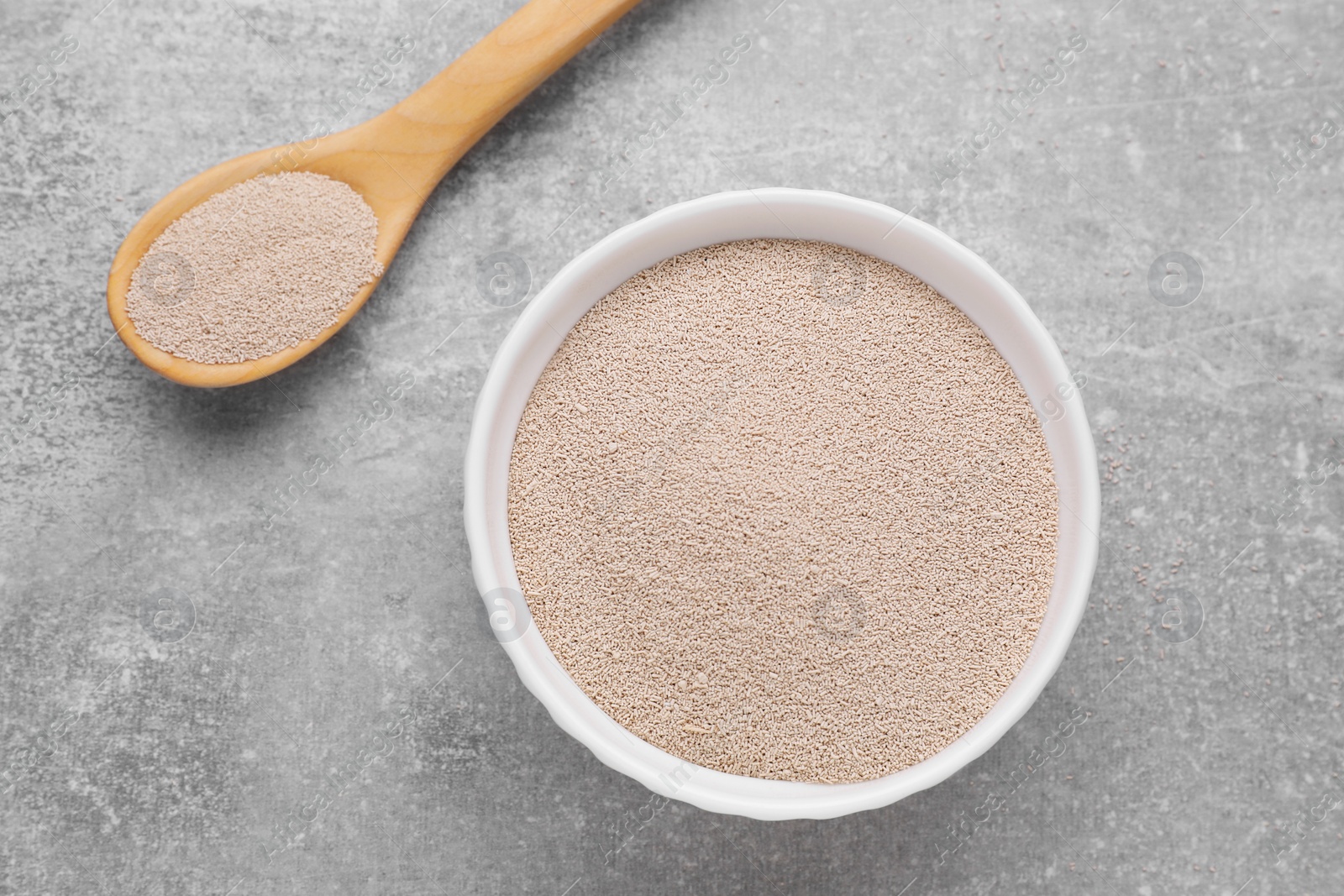 Photo of Bowl and spoon with active dry yeast on light grey table, closeup, flat lay