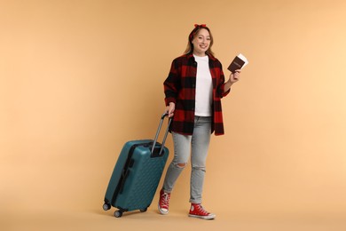 Happy young woman with passport, ticket and suitcase on beige background