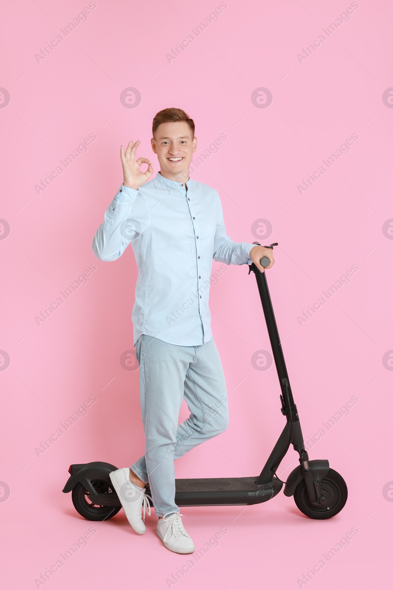 Photo of Happy man with modern electric kick scooter showing OK gesture on pink background