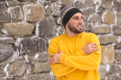 Photo of Young man wearing warm clothes outdoors near stone wall. Winter vacation