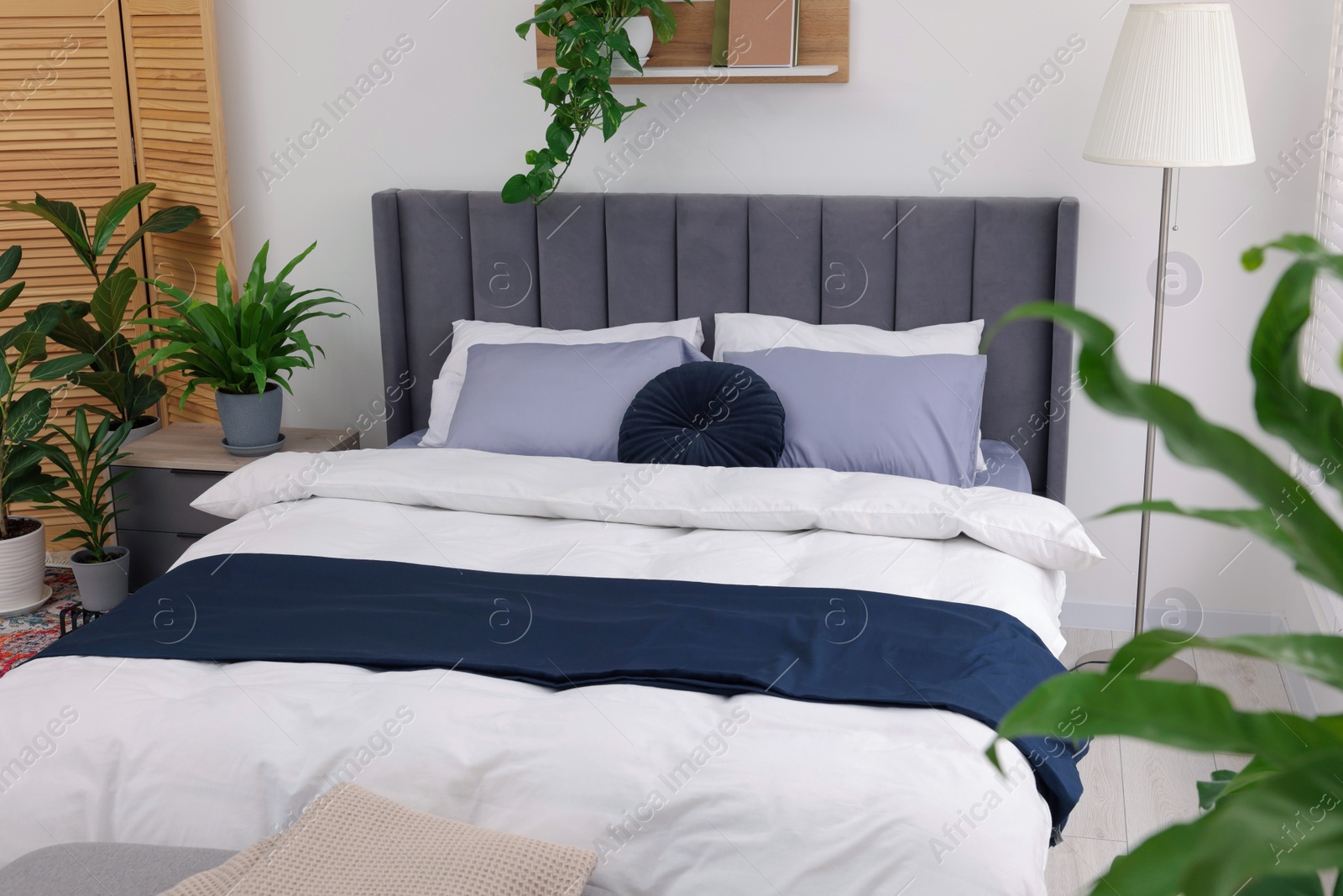 Photo of Beautiful green houseplants and bed in room. Bedroom interior