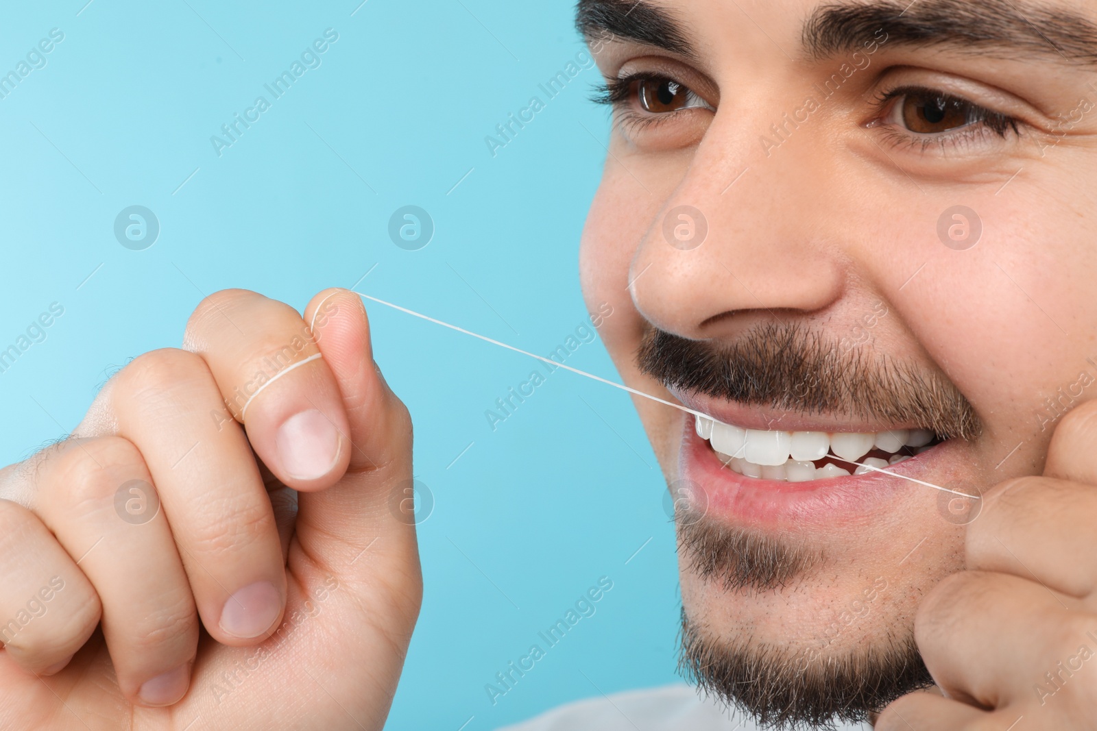 Photo of Young man flossing teeth on color background, closeup