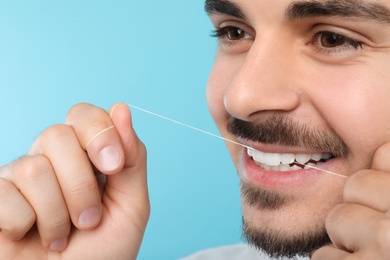 Photo of Young man flossing teeth on color background, closeup