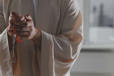 Photo of Muslim man with misbaha near window indoors, closeup. Space for text