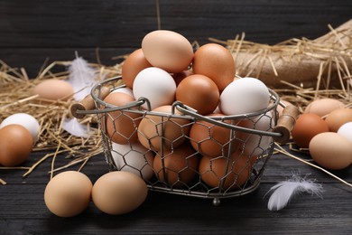 Photo of Fresh chicken eggs and dried straw on black wooden table