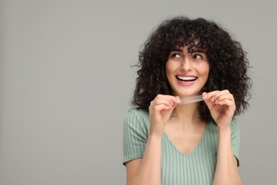 Young woman holding teeth whitening strip on grey background, space for text