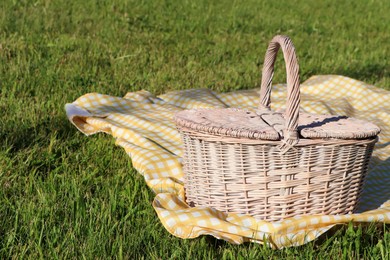 Picnic basket with checkered tablecloth on green grass outdoors, space for text