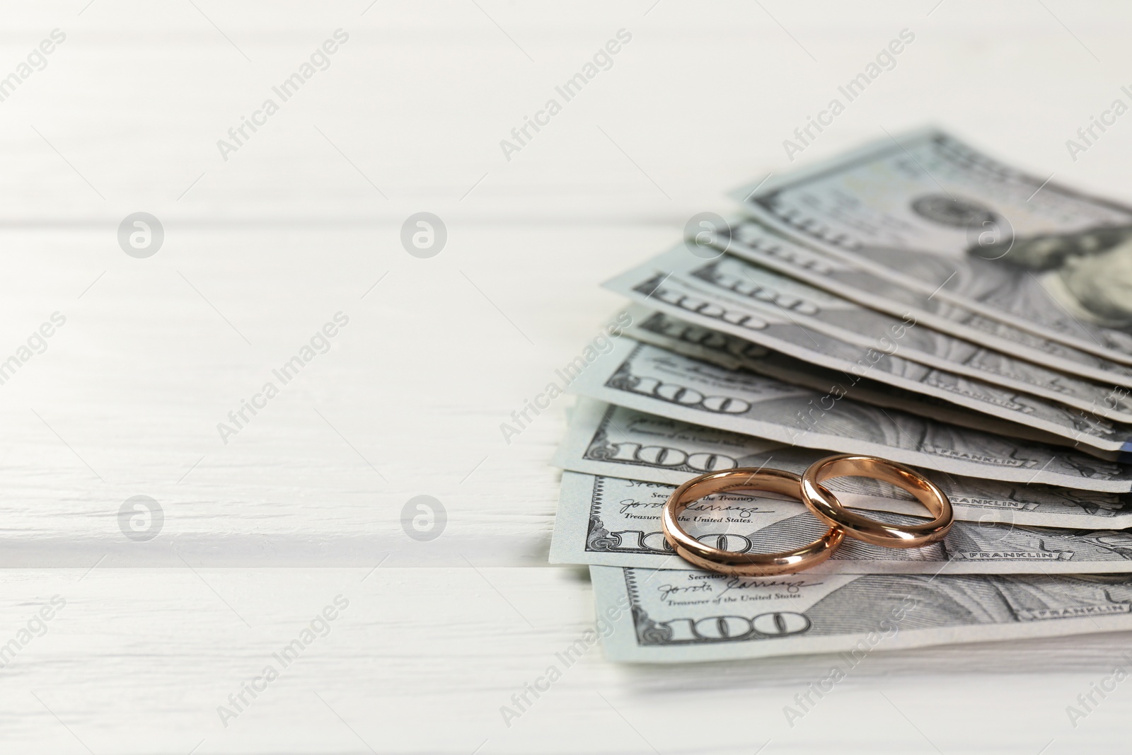 Photo of Honeymoon concept. Dollar banknotes and golden rings on white wooden table, closeup. Space for text