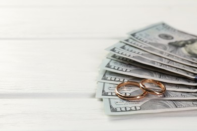 Honeymoon concept. Dollar banknotes and golden rings on white wooden table, closeup. Space for text