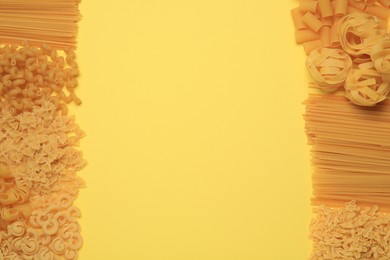 Photo of Different types of pasta on yellow background, flat lay. Space for text