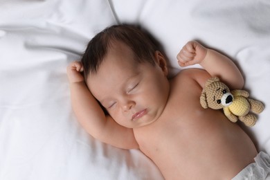Cute little baby with toy bear sleeping on soft bed, top view