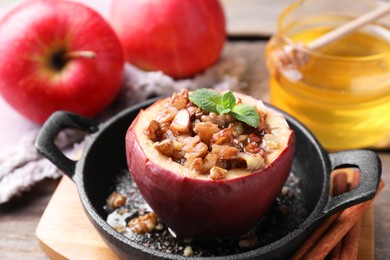 Tasty baked apple with nuts, honey and mint in baking dish on table, closeup