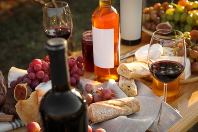 Photo of Red wine and snacks served for picnic on wooden table outdoors