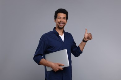 Photo of Happy man with laptop showing thumb up on grey background