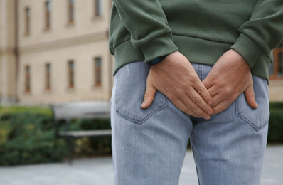 Photo of Man suffering from hemorrhoid pain outdoors, back view