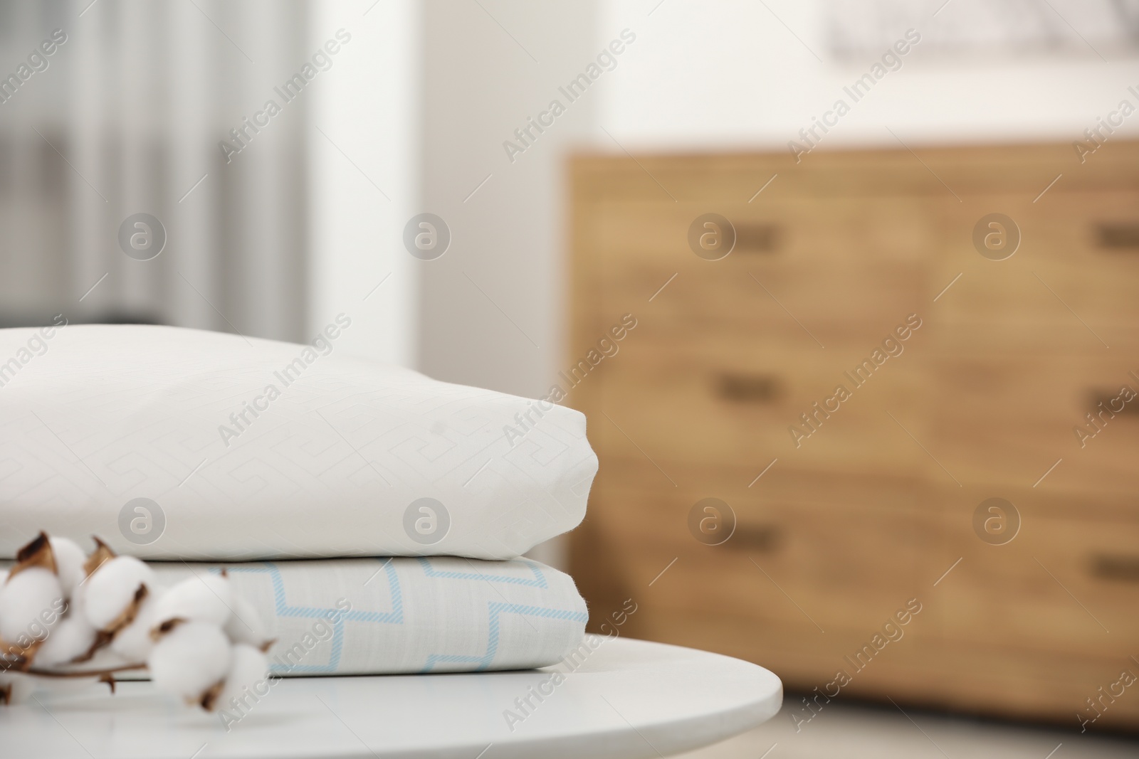 Photo of Bed sheets and cotton branch with fluffy flowers on white table in room, closeup. Space for text